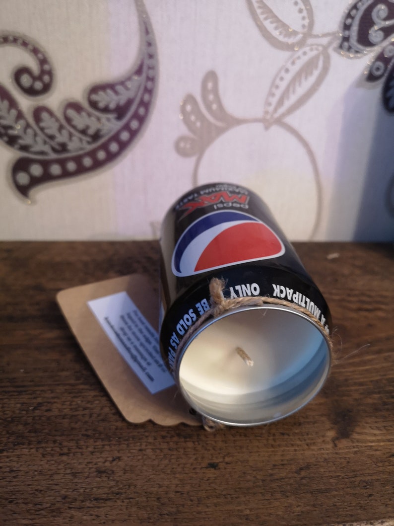 May include: Black and red soda can candle with a white wax interior and a brown twine bow. The can has the text "Pepsi" and "Be Sold As Multipack Only" printed on it.