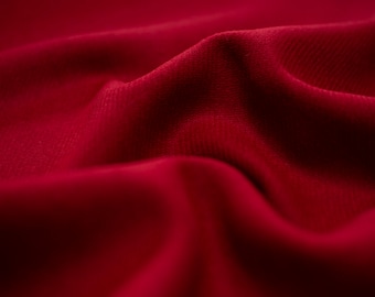 May include: Close-up of deep red fabric with soft folds and subtle textures. The material appears to be a luxurious textile, possibly velvet or a similar plush material. The lighting highlights the curves and shadows.