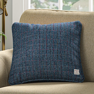 Peut inclure: Un coussin de décoration en tissu bleu et rouge à carreaux avec une texture tweed subtile. Le coussin est posé sur un canapé beige.