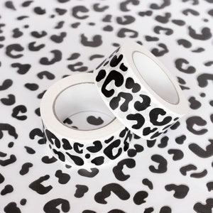 May include: Two rolls of white washi tape with a black leopard print design. The tape is on a white background with a black leopard print.