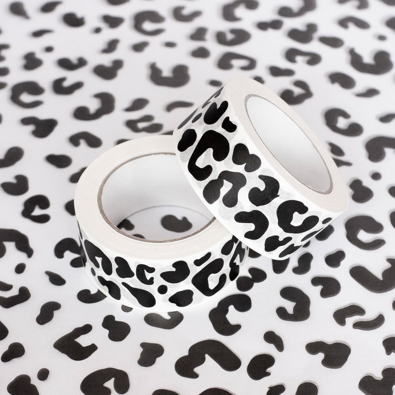 May include: Two rolls of white washi tape with a black leopard print design. The tape is on a white background with a black leopard print.