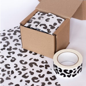 May include: A cardboard box with a leopard print tissue paper lining. The box is being taped shut with a leopard print tape dispenser.