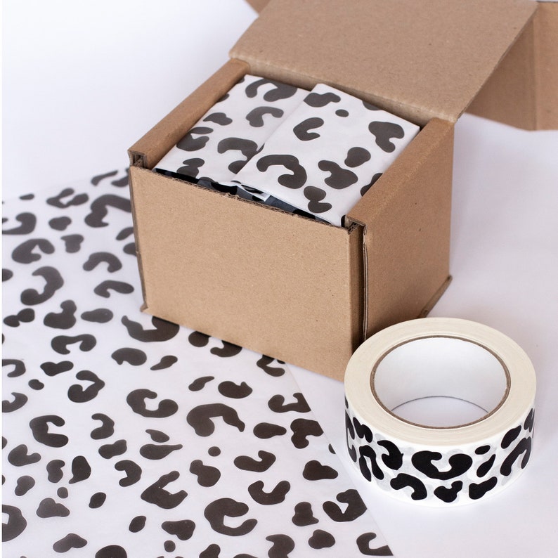 May include: A cardboard box with a leopard print tissue paper lining. The box is being taped shut with a leopard print tape dispenser.
