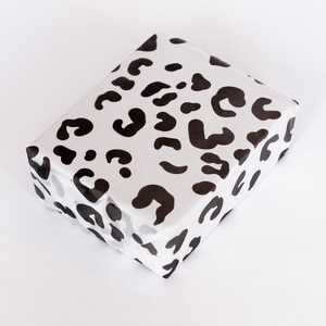 May include: White gift wrapping paper with a black leopard print pattern.