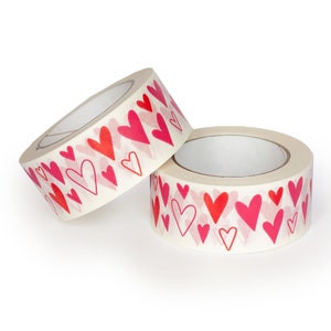 Puede incluir: Dos rollos de cinta adhesiva decorativa con un patr&oacute;n repetido de corazones rojos y rosas. La cinta es de color blanco roto y los corazones var&iacute;an en tama&ntilde;o y estilo. Ideal para manualidades y envolver regalos.