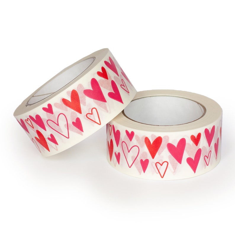 Puede incluir: Dos rollos de cinta adhesiva decorativa con un patr&oacute;n repetido de corazones rojos y rosas. La cinta es de color blanco roto y los corazones var&iacute;an en tama&ntilde;o y estilo. Ideal para manualidades y envolver regalos.