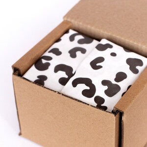 May include: A cardboard box with a lid open, revealing a white tissue paper with a black leopard print pattern inside.