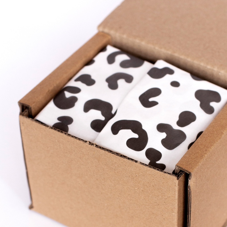 May include: A cardboard box with a lid open, revealing a white tissue paper with a black leopard print pattern inside.