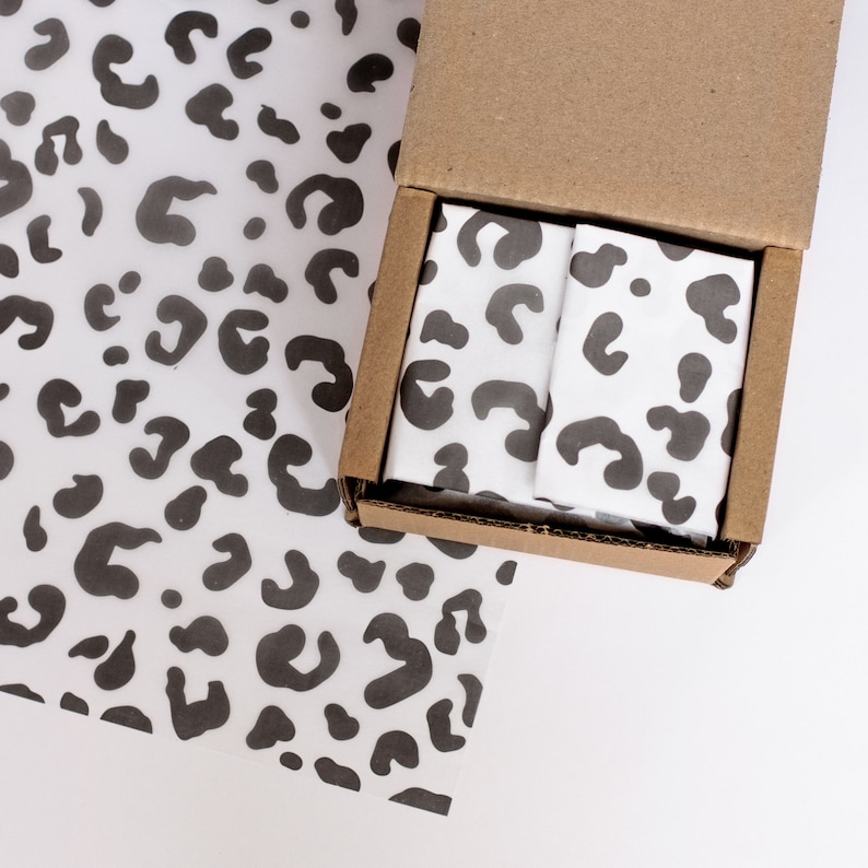 May include: A brown cardboard box with a white and black leopard print tissue paper inside. The tissue paper is folded neatly and the box is open.