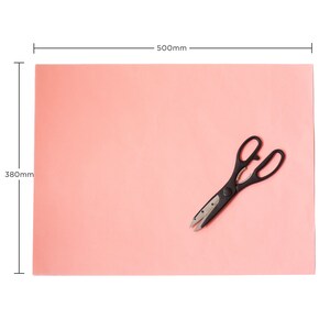 May include: A pink sheet of paper measuring 380mm by 500mm with a pair of black kitchen shears on top.