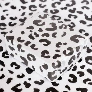 May include: White wrapping paper with a black leopard print pattern. The paper is folded and has a slight sheen.
