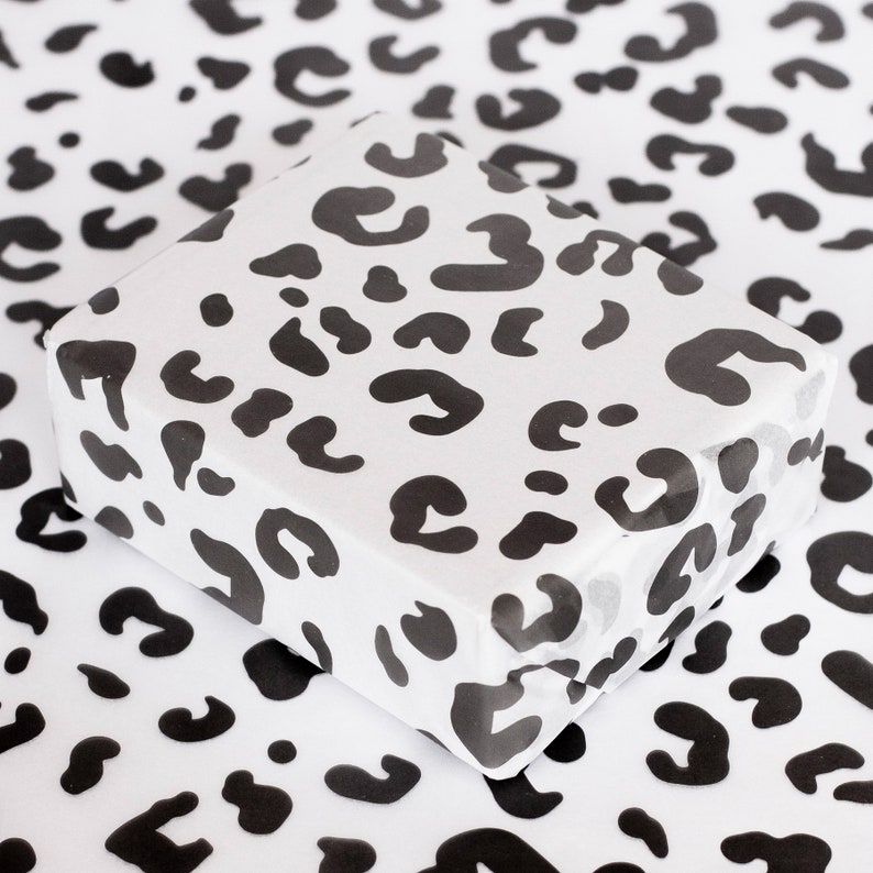 May include: White wrapping paper with a black leopard print pattern. The paper is folded and has a slight sheen.