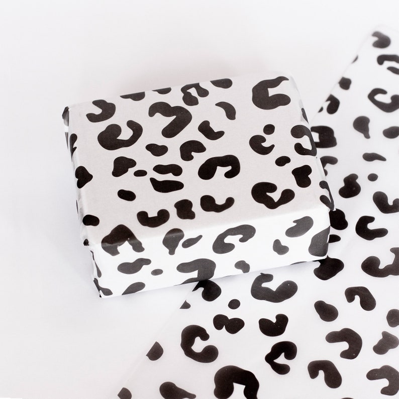 May include: A white gift box with a black leopard print design. The box is wrapped in white tissue paper with the same leopard print design.