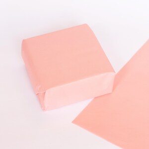 May include: A pale pink square box made of tissue paper, sitting on a larger sheet of pale pink tissue paper.