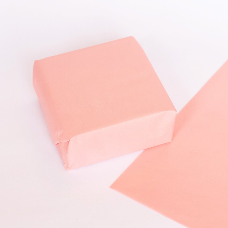 May include: A pale pink square box made of tissue paper, sitting on a larger sheet of pale pink tissue paper.