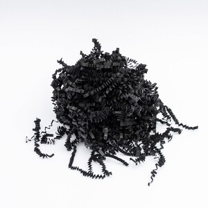 May include: A pile of black crinkle paper, a decorative filler for gift boxes and packaging. The shredded paper has a textured, wavy appearance and is arranged against a white background.