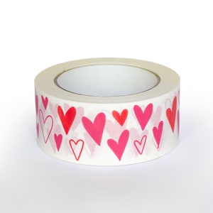 Puede incluir: Un rollo de cinta adhesiva decorativa con un patr&oacute;n repetido de corazones rojos y rosas sobre un fondo blanco. Los corazones var&iacute;an en tama&ntilde;o y estilo, algunos delineados y otros s&oacute;lidos.