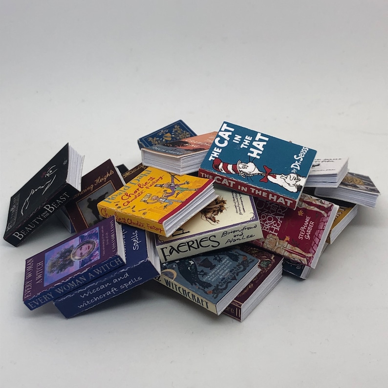 Puede incluir: Una colecci&oacute;n de libros en miniatura con varios t&iacute;tulos, incluyendo "El Gato en el Sombrero", "Every Woman a Witch", "Hadas" y "No Broken Heart". Los libros est&aacute;n apilados y dispuestos en una pila, mostrando una variedad de colores y dise&ntilde;os.