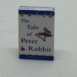Puede incluir: Un libro de bolsillo vintage titulado "The Tale of Peter Rabbit" de Beatrix Potter. La portada presenta una ilustraci&oacute;n azul y blanca de un conejo con una chaqueta azul, volando por el aire.