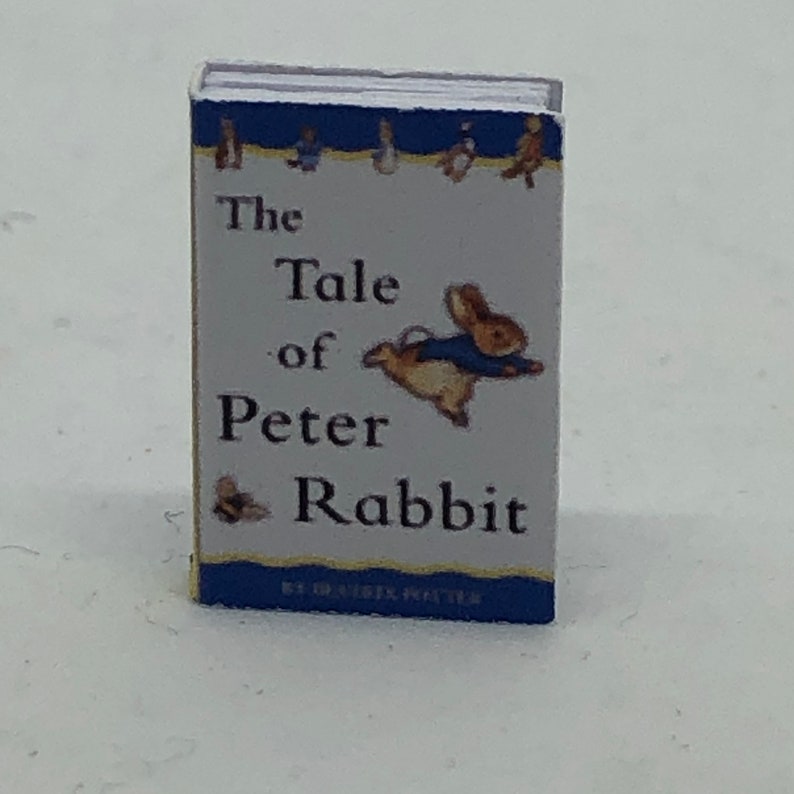 Puede incluir: Un libro de bolsillo vintage titulado "The Tale of Peter Rabbit" de Beatrix Potter. La portada presenta una ilustraci&oacute;n azul y blanca de un conejo con una chaqueta azul, volando por el aire.