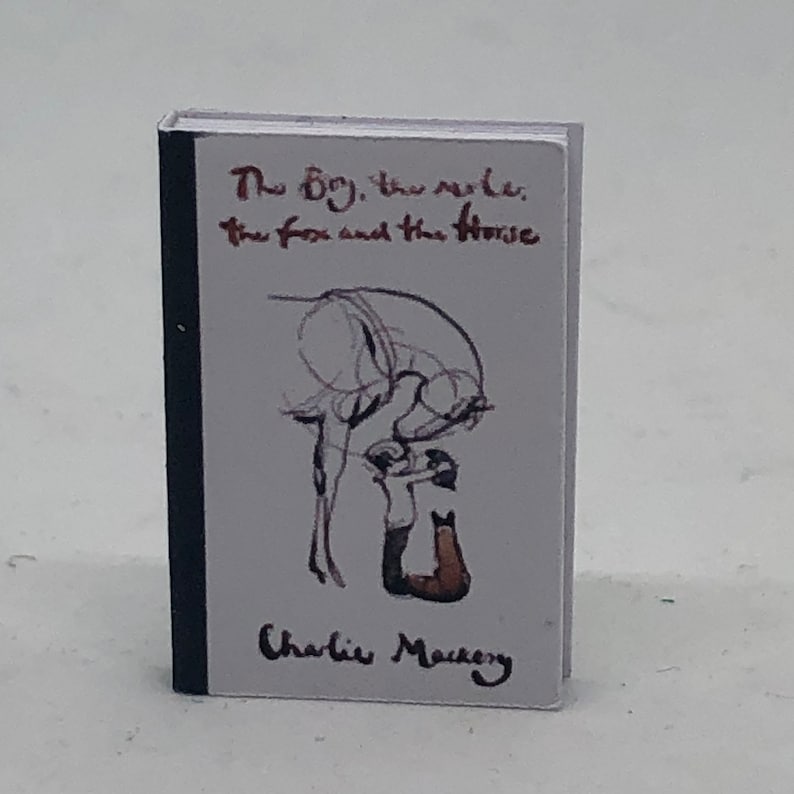 Puede incluir: Un libro blanco con una encuadernaci&oacute;n negra. La portada presenta una ilustraci&oacute;n en blanco y negro de un ni&ntilde;o acariciando un caballo. El t&iacute;tulo del libro es "The Boy, the Mole, the Fox and the Horse" de Charlie Mackesy.