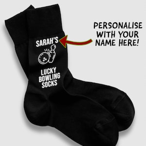 May include: A pair of black socks with white text and a bowling-themed graphic. The text reads "SARAH'S" above a bowling pin and ball illustration, with "LUCKY BOWLING SOCKS" below. The socks are personalized with the name "SARAH'S".