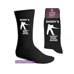 Puede incluir: Calcetines negros con una silueta blanca de una persona jugando al billar y el texto "Daddy's Lucky Pool Socks".