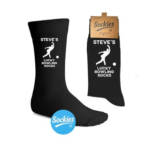 May include: Black socks with the text "STEVE'S LUCKY BOWLING SOCKS" and a white graphic of a bowler. The socks have a blue and white "Sockies" logo on the side. A tag with the "Sockies" logo is attached to the socks.