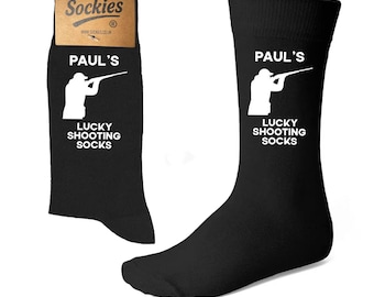 May include: Black socks with the text "PAUL'S LUCKY SHOOTING SOCKS" in white. The socks feature a white silhouette of a person aiming a rifle. The packaging reads "Sockies".