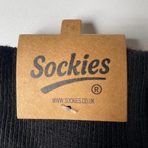 May include: Close-up of a brown cardboard tag with the word "Sockies" in black script. Below the word is a curved line and the registered trademark symbol. The website address www.sockies.co.uk is printed below.