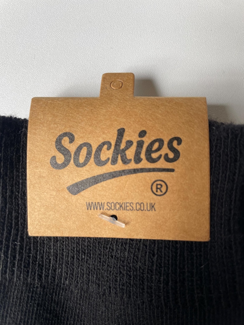May include: Close-up of a brown cardboard tag with the word "Sockies" in black script. Below the word is a curved line and the registered trademark symbol. The website address www.sockies.co.uk is printed below.