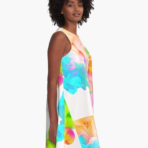 May include: A white sleeveless dress with a colorful abstract design featuring blue, green, yellow, pink, and orange. The design resembles paint splatters or ink blots.