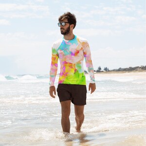 K&ouml;nnte beinhalten: Eine Person tr&auml;gt ein lang&auml;rmeliges Shirt mit einem farbenfrohen abstrakten Druck und schwarze Badehosen. Das Shirt hat einen wei&szlig;en Untergrund mit einem farbenfrohen abstrakten Design in Pink, Gelb, Blau und Gr&uuml;n.