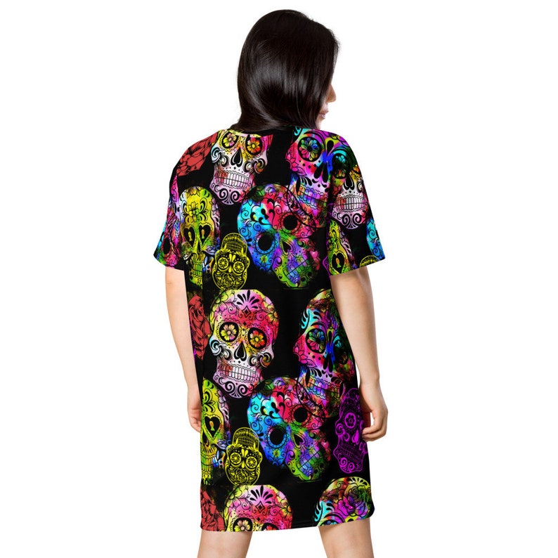 May include: Black t-shirt dress with a colorful sugar skull pattern. The skulls are decorated with flowers and have a vibrant, psychedelic look.