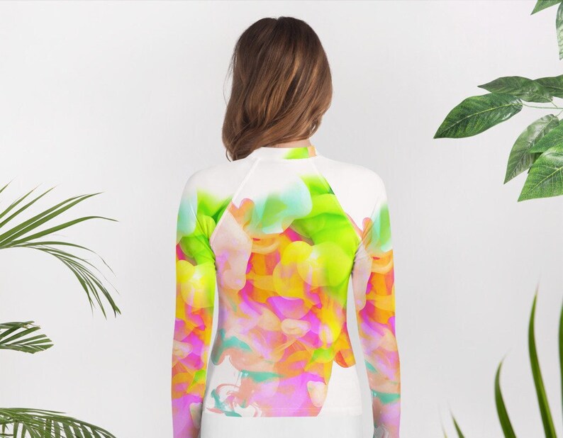 May include: White long-sleeve rash guard with a colorful abstract design featuring pink, yellow, green, and blue hues.