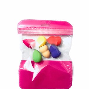 Może przedstawiać: Przezroczysty plastikowy worek z r&oacute;żowym zamkiem błyskawicznym zawiera sześć kolorowych gąbek do makijażu. Gąbki są w r&oacute;żnych kształtach i rozmiarach, w tym okrągłe, owalne i w kształcie łzy.