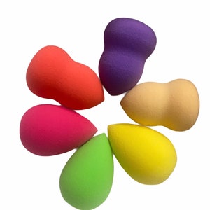 May include: Six colorful makeup sponges in various shapes, including teardrop and round, arranged in a flower-like pattern.