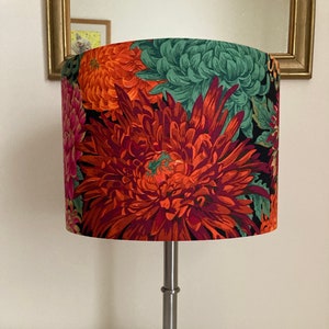 May include: A silver table lamp with a floral patterned lampshade. The lampshade features large red, orange, and green flowers on a black background.