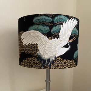 May include: A black and gold table lamp with a white crane and pine tree design on the lampshade.