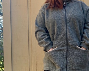 May include: A gray fleece jacket with a zipper closure and two large pockets. The jacket is worn over black biker shorts.