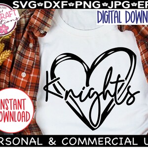 May include: A white t-shirt with a black heart design and the word "Knights" written inside the heart. The design is on a white t-shirt with a red and black checked shirt folded on top of it.