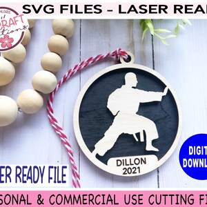 May include: A laser-cut wooden ornament featuring a silhouette of a person in a karate pose. The ornament is black with a white silhouette and the text "Dillon 2021".