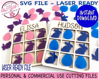 May include: Two wooden Easter-themed Tic Tac Toe boards with the names "Elissa" and "Hudson" on them. The boards have nine squares each, with bunny and egg shapes cut out. There are also loose bunny and egg shapes in pink, purple, and blue.