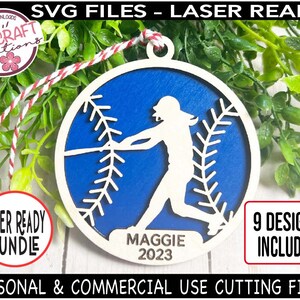 May include: A blue and white baseball-themed wooden ornament with a silhouette of a softball player and the text "MAGGIE 2023".