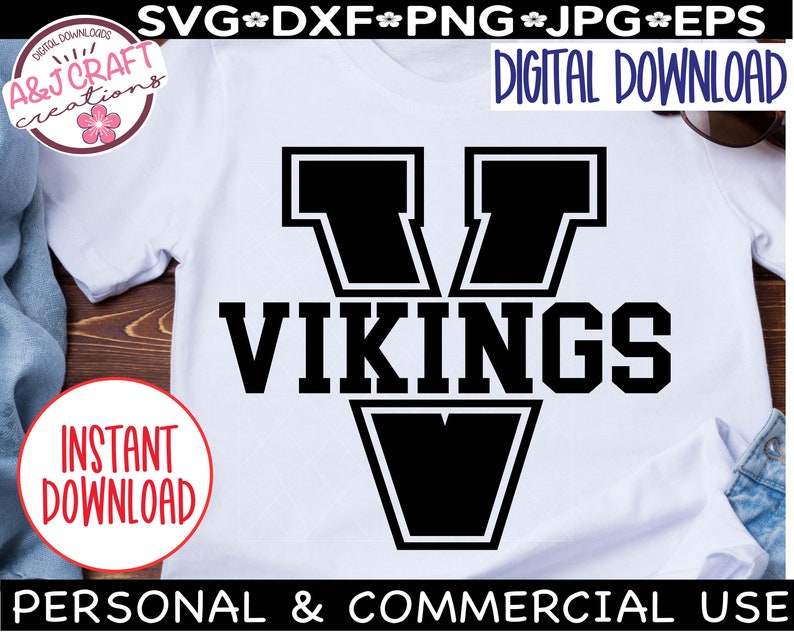 May include: A white t-shirt with a black graphic of a large letter V with the word "VIKINGS" underneath. The graphic has a thick black outline.