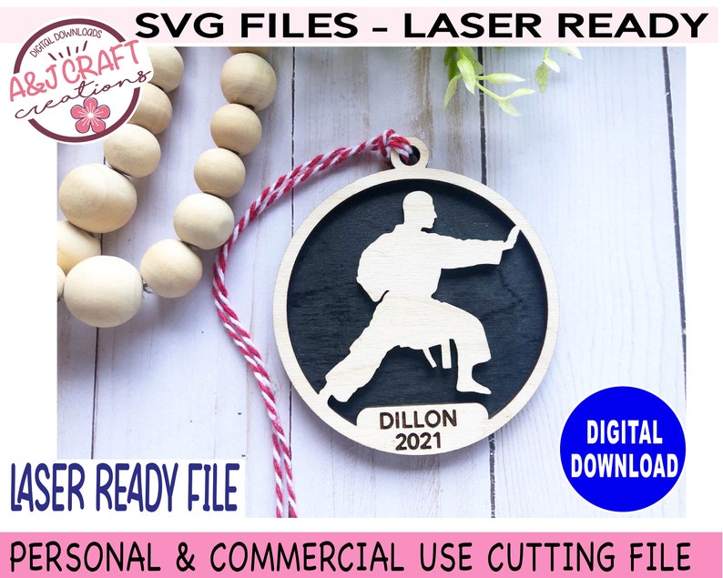 May include: A laser-cut wooden ornament featuring a silhouette of a person in a karate pose. The ornament is black with a white silhouette and the text "Dillon 2021".