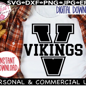 May include: A white t-shirt with a black graphic of a large letter V with the word "VIKINGS" underneath. The graphic is outlined in white. The t-shirt is on a plaid shirt.