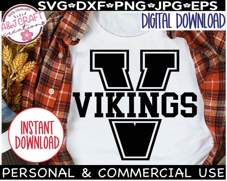 May include: A white t-shirt with a black graphic of a large letter V with the word "VIKINGS" underneath. The graphic is outlined in white. The t-shirt is on a plaid shirt.
