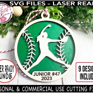 May include: A green and white laser cut wooden ornament featuring a softball player silhouette. The ornament is round and has a baseball stitching pattern. The text "JUNIOR #47 2023" is printed on the ornament.