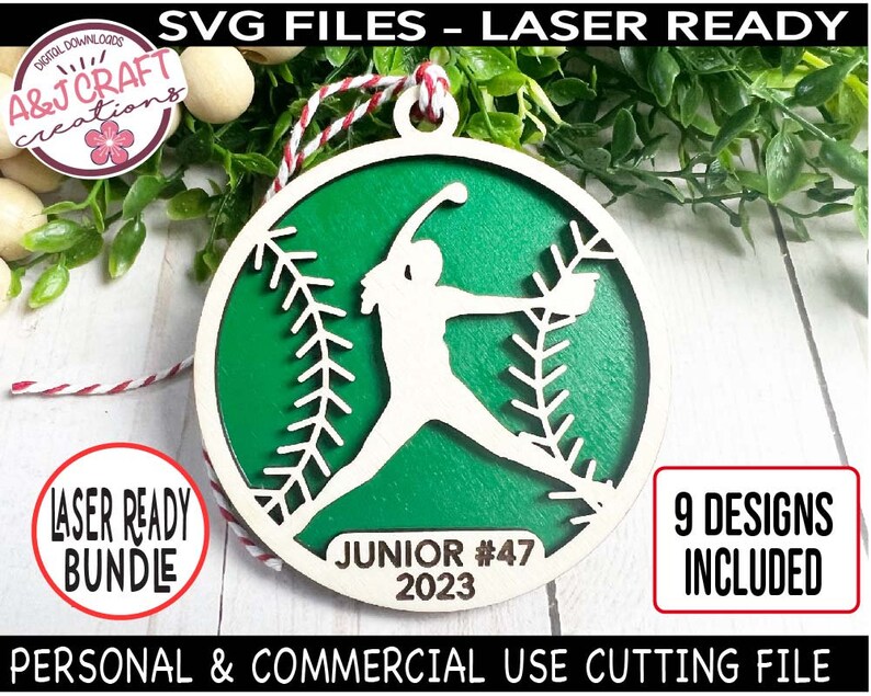 May include: A green and white laser cut wooden ornament featuring a softball player silhouette. The ornament is round and has a baseball stitching pattern. The text "JUNIOR #47 2023" is printed on the ornament.